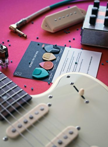 A flat lay of guitar picks, cables, and guitar parts on a pink background.