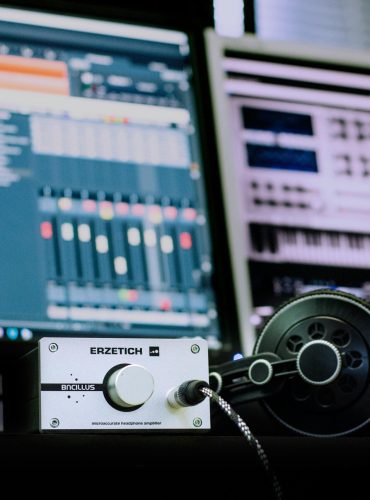 Close-up of a professional music studio setup featuring an amplifier and headphones with digital audio workstations in the background.