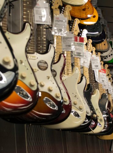 Row of colorful electric guitars hanging in a music store, showcasing diverse models and prices.